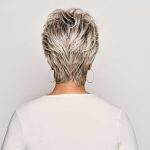 Back view of a woman with short, layered gray wig and hoop earrings.