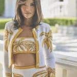 Woman wearing a white and gold palm print cardigan and matching shorts outside.
