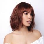 Red wavy wig on a woman with shoulder-length hair and bangs.