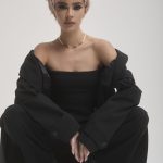 Fashion model with short pink hair, black outfit, and stylish pose for Hidden Secrets Wigs.