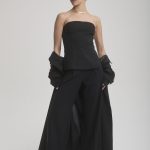 Fashion model with short pink hair in black outfit and wide-leg pants.
