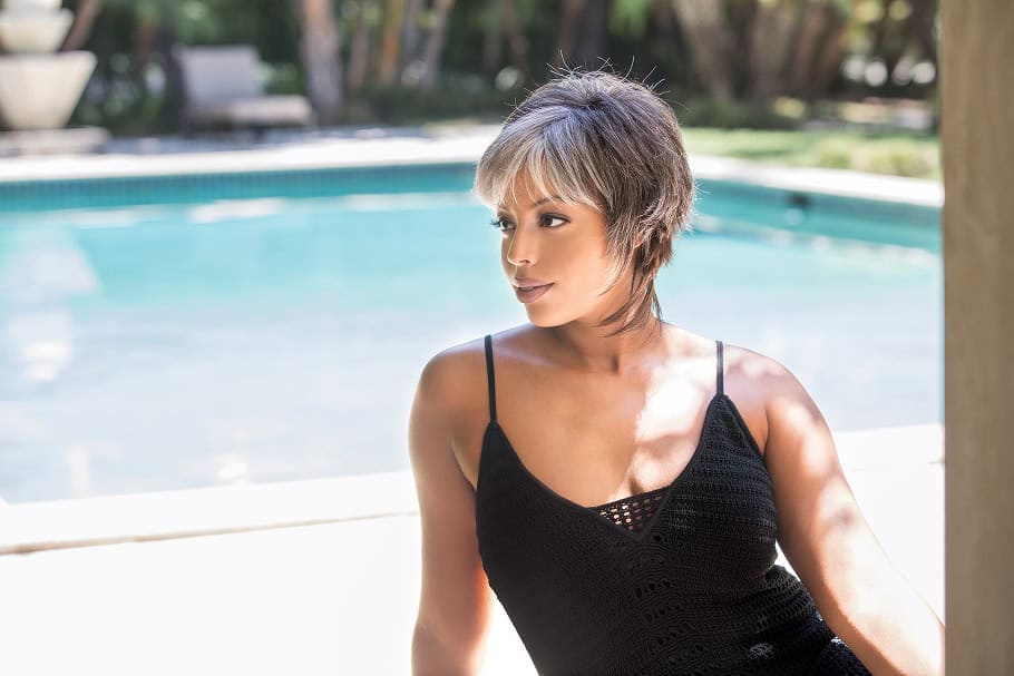Woman with short gray wig by poolside in sunlight.