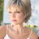 Woman with short blonde wig and leaf earrings outdoors.