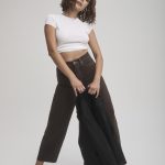 Fashion model with curly hair wearing a white crop top and black pants.