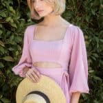 Blonde bob wig styled on a woman in pink dress holding a straw hat.