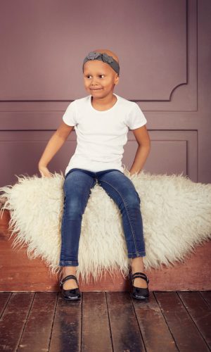 Young girl sitting on a fluffy white rug with a purple wall background.