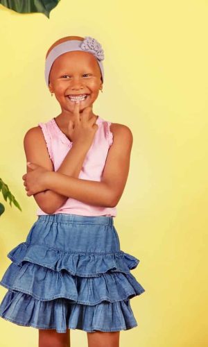 Young girl smiling with a wig and summer outfit, tropical background.