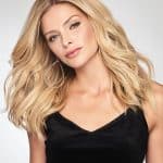 Blonde wavy wig styled on a woman with black top and hoop earrings.