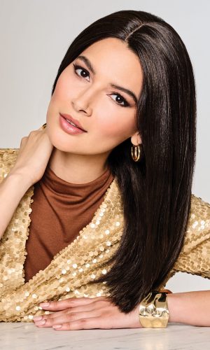 Woman with long, straight black wig, gold earrings, and gold bracelet.