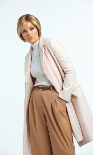 Woman with short blonde wig in a professional outfit against a white background.