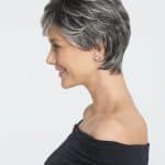 Side view of a woman with short, layered gray wig and earrings.