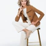 Woman with blonde wavy wig, casual outfit, sitting on a stool.