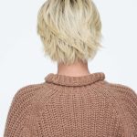 Blonde layered short wig viewed from the back on a woman in a brown sweater.
