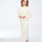 Woman in cream sweater and skirt with wavy hair, posing against white background.