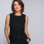 Woman with short brown wig, wearing black sleeveless top, smiling confidently.
