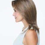 Side view of a woman wearing a light brown wavy wig.