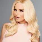 Blonde wavy wig styled on a woman with flawless makeup and a soft pink top.