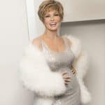 Woman with short wavy blonde wig wearing a silver dress and white fur coat.