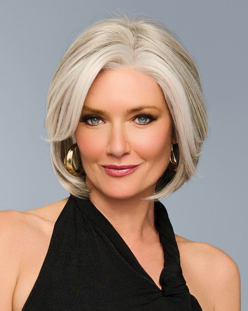 Woman with stylish silver bob wig and hoop earrings, smiling confidently.