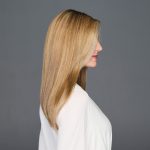 Side view of a woman with long, straight blonde wig against gray background.