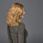 Side view of a woman with wavy blonde wig, gray background.