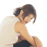 Woman with short brown wavy wig, casual beige top, sitting pose.