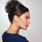 Side profile of a woman with a curly updo wig and sleek dark hair.