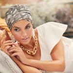 Woman wearing a boho turban and jewelry, relaxing on a sofa.
