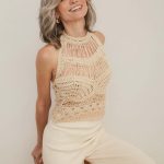 Elegant woman with silver wig, wearing a crochet top and cream pants, smiling.