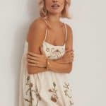 Blonde woman with wavy hair wearing a floral dress, posing against a white background.
