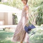 Woman in a leopard print dress holding a blue hat outdoors.