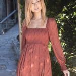 Blonde wig styled on a woman in a rust-colored dress outdoors.