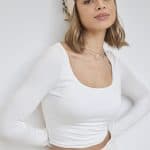 Model wearing a wavy bob wig with a beige headscarf, casual white top, and confident expression.