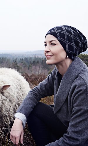 Woman wearing a winter hat outdoors with sheep in the background.
