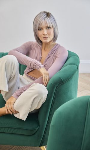 Elegant woman with silver bob wig sitting on green sofa.
