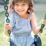 Happy young girl on a swing set smiling at the camera.