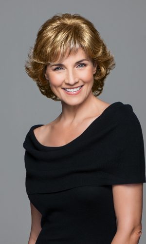 Woman with short, wavy blonde wig smiling at camera.
