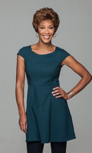 Smiling woman with short curly wig in teal dress, posing confidently.