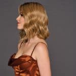 Wavy blonde wig on a woman with side profile against gray background.