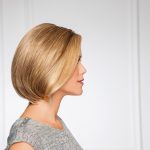 Side view of a woman with a sleek blonde bob wig in a bright room.