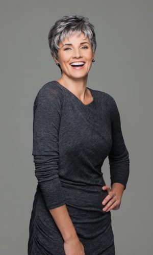 Smiling mature woman with short gray wig and casual dark gray outfit.