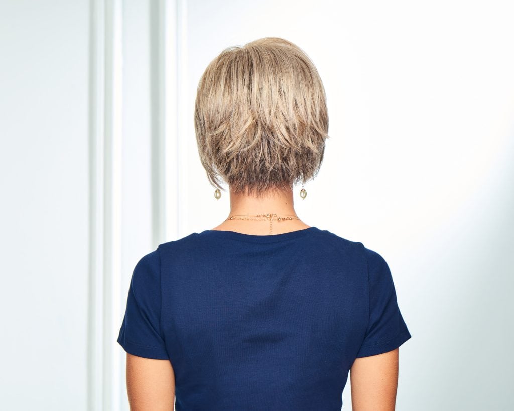 Back view of a woman with a short blonde wig and blue top.