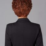 Close-up of a woman with a curly red wig, back view, in a black blazer.