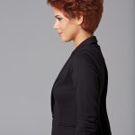 Side view of a woman with short, curly red wig and black blazer.