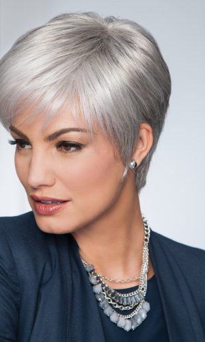 Woman with short silver wig, stylish and elegant, wearing a navy blazer and jewelry.