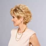Side view of a woman with a short, layered blonde wig and gold jewelry.