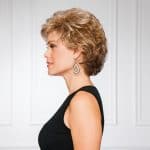 Side view of a woman with short, curly, blonde wig and earrings.