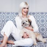 Happy blonde woman with a dog sitting on a patterned sofa.