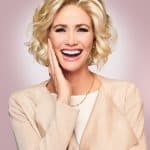 Happy woman with blonde curly wig, smiling and touching her face.