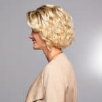 Blonde curly wig styled on a woman with side profile view.